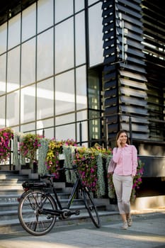 Young woman standing near ebike and uses smartphone outdoor