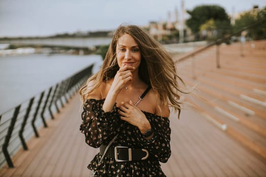 Pretty young long hair brunette woman walking on the riverside