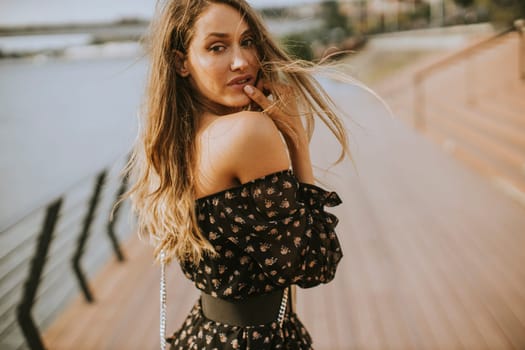 Pretty young long hair brunette woman walking on the riverside