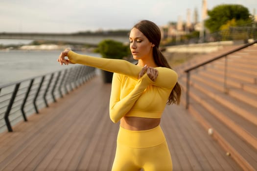 Pretty young woman having stretching exercise on the riverside pier