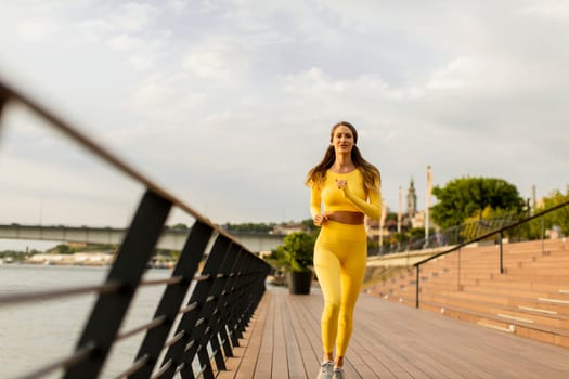 Pretty young woman running exercise on the riverside pier