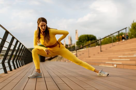 Pretty young woman having stretching exercise on the riverside pier