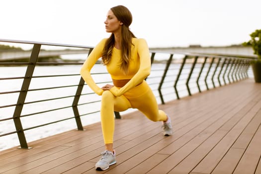 Pretty young woman having stretching exercise on the riverside pier