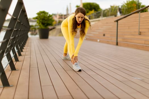 Pretty young woman having stretching exercise on the riverside pier