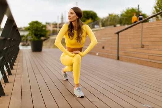 Pretty young woman having stretching exercise on the riverside pier