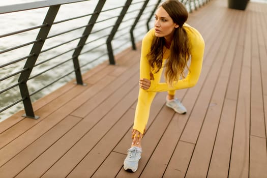 Pretty young woman having stretching exercise on the riverside pier