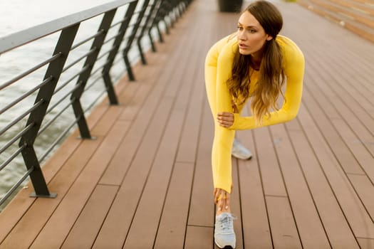 Pretty young woman having stretching exercise on the riverside pier