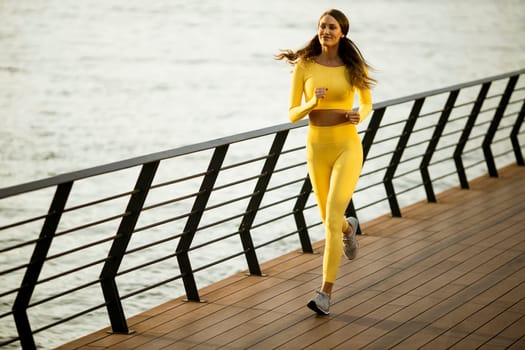 Pretty young woman taking running exercise by the river promenade