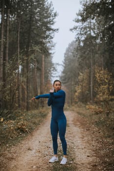 Pretty young woman in blue track suit stretching before workout in the autumn forest