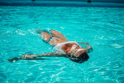 Woman relaxing swimming pool. Happy woman in a blue swimsuit floating in the pool, look form above.