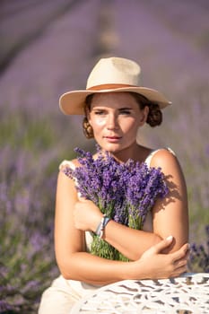 A woman is sitting in a field of lavender flowers and wearing a straw hat. She is smiling and holding a bouquet of flowers. Scene is peaceful and serene, as the woman is surrounded by the beauty of nature.