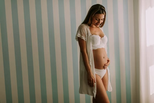 Pretty young pregnant woman standing by the wall in the room
