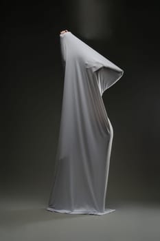 A woman playfully showcases her beauty while draped in soft, sheer fabric against a dark background.