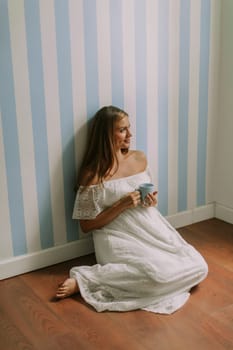 Pretty young pregnant woman sitting on a floor by the wall in the room