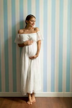 Pretty young pregnant woman standing by the wall in the room
