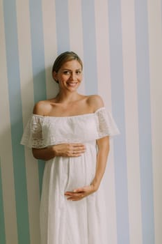 Pretty young pregnant woman standing by the wall in the room