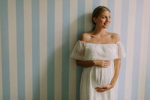 Pretty young pregnant woman standing by the wall in the room