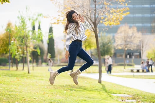 A joyful and spirited young woman dressed in stylish casual clothes leaps with excitement in a vibrant park, vividly capturing the essence of fun, freedom, and enjoyment found in leisure activities
