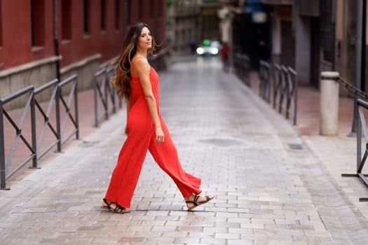 In a vibrant city, a fashionable woman confidently walks down a tranquil street in a striking red jumpsuit, showcasing her unique style and elegance, captivating everyone with her grace and poise