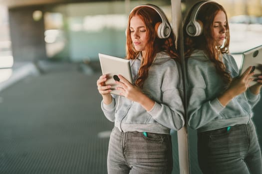 A young woman with vibrant red hair is immersed in her music, wearing stylish headphones and holding a sleek tablet, creating a modern, relaxed vibe that feels contemporary and chill
