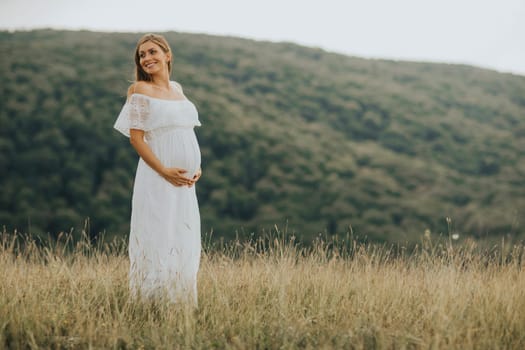 Young pregnant woman relaxing outside in nature at summer day