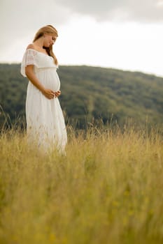 Young pregnant woman relaxing outside in nature at summer day