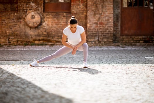 Pretty young woman stretching during training in the urban environment