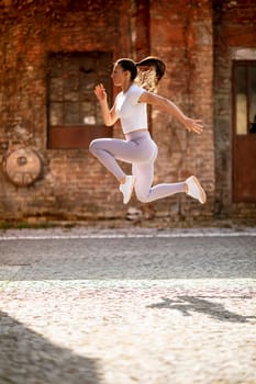 Pretty young woman juping high during training in the urban environment
