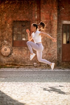 Pretty young woman juping high during training in the urban environment