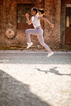 Pretty young woman juping high during training in the urban environment