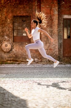 Pretty young woman juping high during training in the urban environment