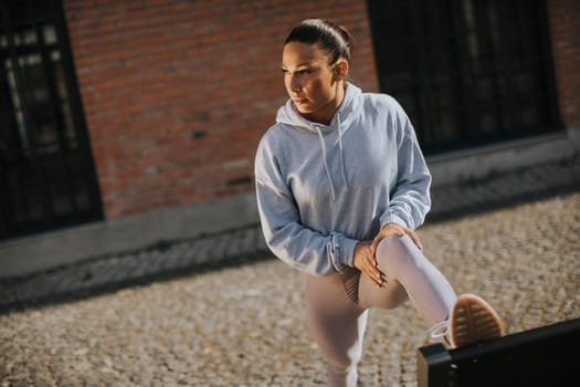 Pretty young woman stretching during training in the urban environment