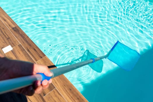 Close-up of skimmer net cleaning turquoise water in swimming pool with wooden deck