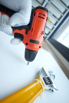 A close view of a hand operating a power drill near a wrench.