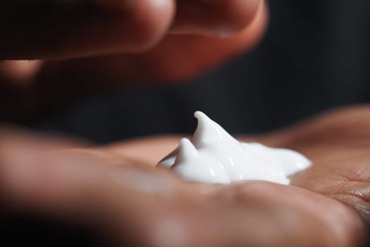 A hand holds a small amount of cream, ready for skincare application.