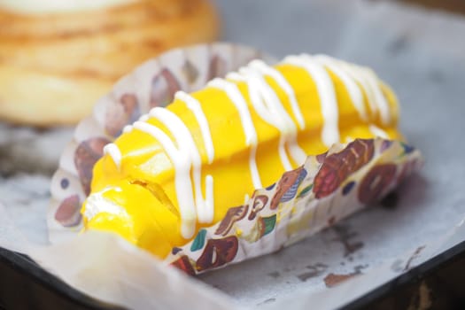 A yellow dessert drizzled with white cream in a paper wrapper.