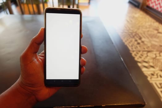 A hand is seen holding a blank smartphone at a cafe table.