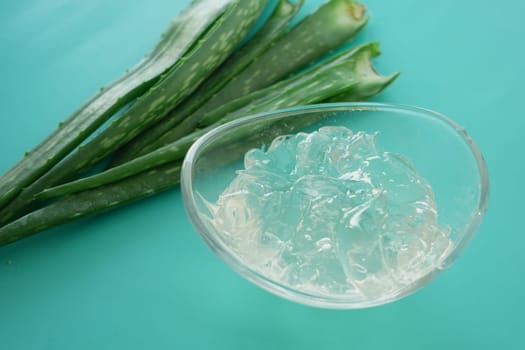 Clear aloe vera gel is placed beside fresh aloe leaves on a bright surface.