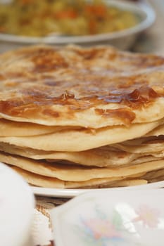 Soft flatbreads stacked high on a plate in a warm kitchen setting.