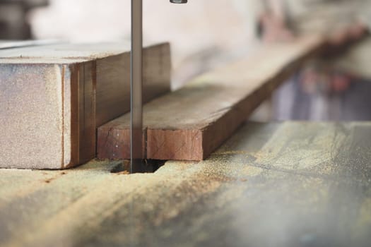 A lumber piece is being cut by a saw in a busy woodworking workshop.