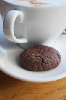 Coffee sits in a white cup beside a chocolate cookie on a plate.