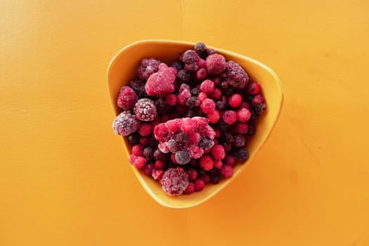A bowl filled with assorted frozen berries sits on a bright surface.