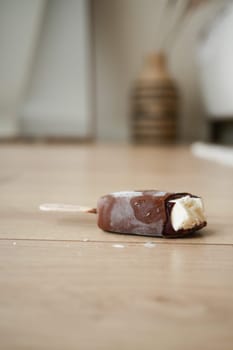 A chocolate-coated popsicle lies on a wooden floor, partially melted.