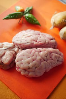 Fresh animal brains are placed on a bright cutting board with herbs.