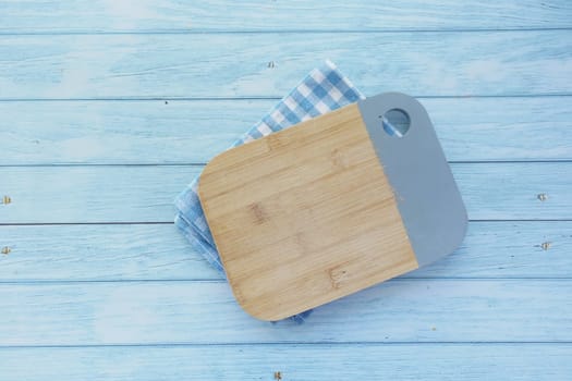 A cutting board rests atop a blue checkered napkin on a wood table.