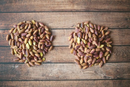 Piles of shelled pistachios are arranged on a rustic wooden surface.