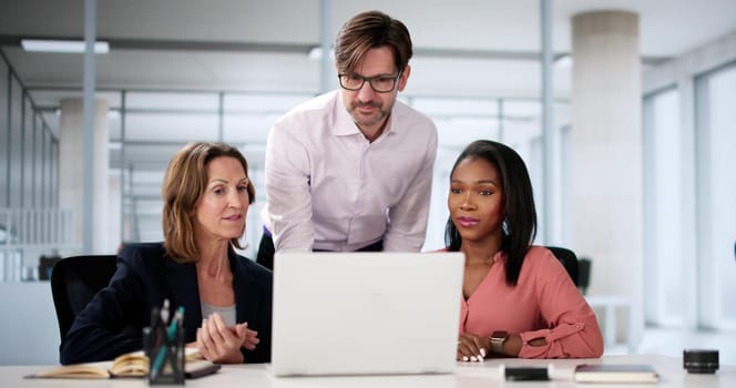 Diverse happy business team collaborating on laptop in office space.