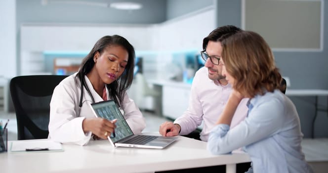 Doctor holding x-ray shows broken knee bone to patient on computer.