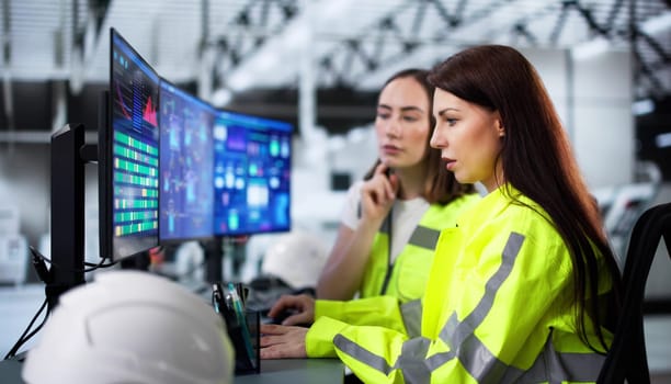 Young woman engineers monitor energy levels on high-tech factory systems.