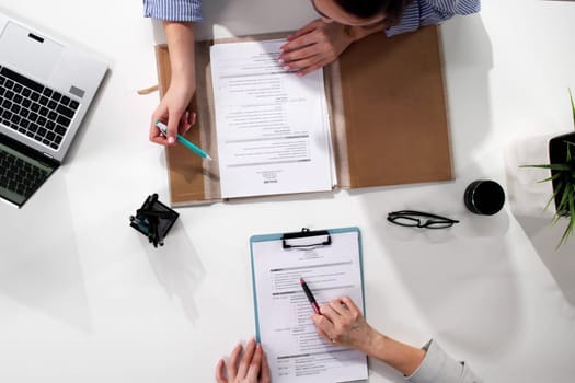 Businesswoman conducting recruiting interview in office, reviewing resumes on computer.